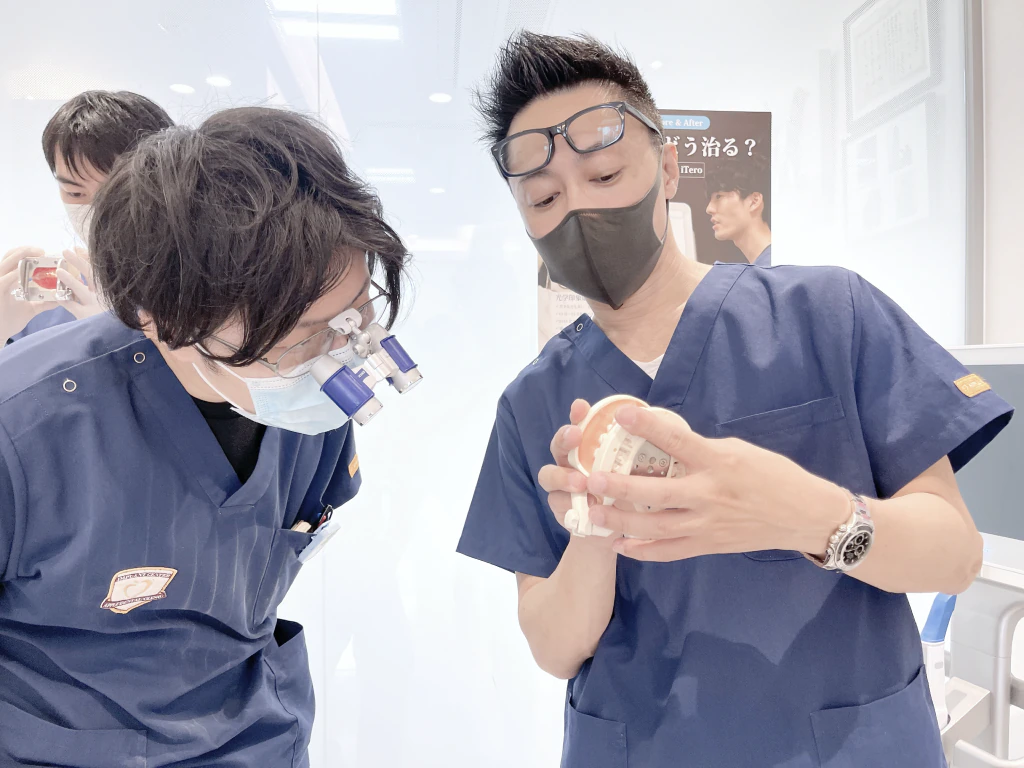 拡大鏡を装着したドクターが歯の模型を使って若手ドクターに指導する様子